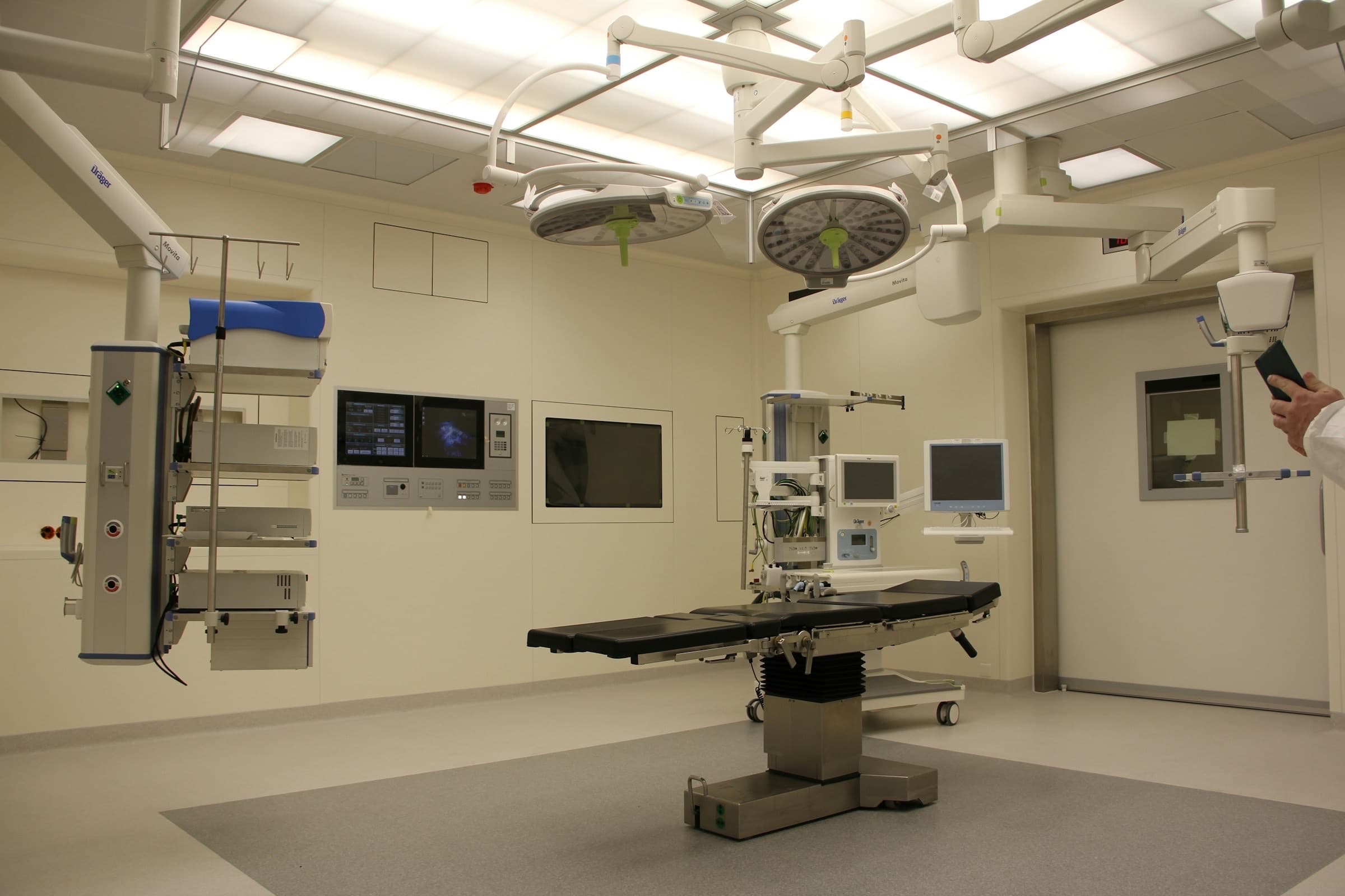 Modern procedure room with a surgical table, overhead lights, and clinical monitors